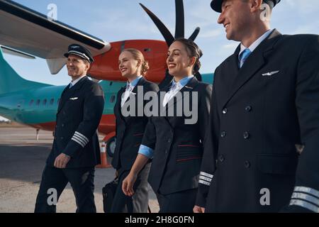 Kabinenpersonal und zwei männliche Piloten, die sich entlang der Flugzeugpiste bewegen Stockfoto