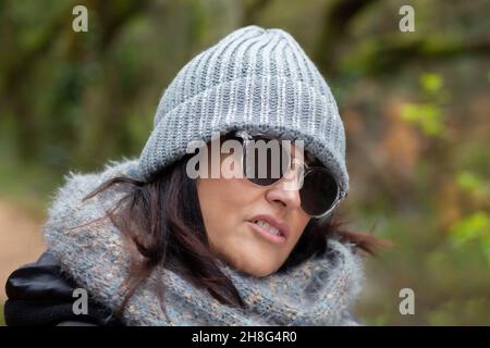 Porträt einer Frau mit Sonnenbrille und Wollhut im Wald an einem Herbsttag am Morgen - Nahaufnahme Porträt Stockfoto