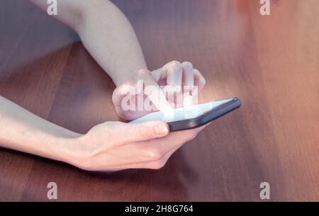 Eine Frau hält ein Mobiltelefon mit einem leeren Bildschirm auf dem Hintergrund eines Holztisches. Mockup-Kopierspeicher. Stockfoto