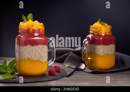 Zwei Gläser mit geschichtetem Chia Pudding auf dunklem Holzhintergrund Stockfoto