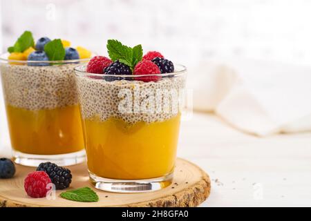 Zwei Gläser Chia Pudding mit Mangopüree und Beeren auf hellem Hintergrund Stockfoto