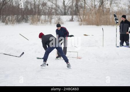 Dnepropetrovsk, Ukraine - 08. Februar 2014: Amateur junger Mann atacking kleinen Tor, wo Senior Mann verteidigen, während Hockey auf einem gefrorenen Fluss spielen Stockfoto