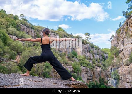 Nicht erkennbare Frau, die Krieger-Asana auf Felsen macht Stockfoto