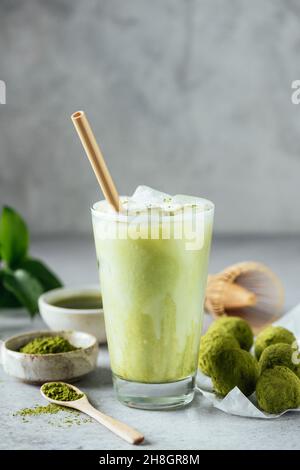 Matcha Ice Latte gesundes veganes Getränk im Glas serviert mit Matcha-Energiebällen. Grauer Hintergrund für Text oder Design Stockfoto