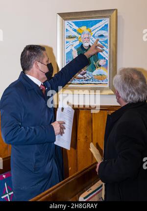 Athestaneford, East Lothian, Schottland, Vereinigtes Königreich, 30th. November 2021. US-Generalkonsul beim Scottish Flag Trust am St. Andrew's Day: Jack Hillmeyer vom US-Konsulat Edinburgh wird am Geburtsort des Saltire zum St. Andrew's Day begrüßt. Im Bild: Jack Hillmeyer sieht eine Darstellung des hl. Andreas mit Provost John McMillan der lokalen Künstlerin Emma Mackenzie, die in der Dorfkirche hängt Stockfoto