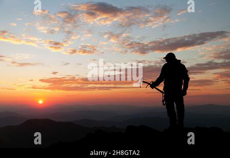 Abendsilhouette - Blick auf den Menschen auf den Bergen mit Eis axt in der Hand Stockfoto