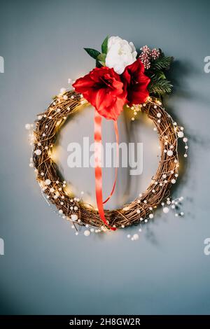 Moderner weihnachtlicher Blumenkranz aus gewebten Ästen, Perlen und Lichtern, die an der grauen Wand hängen. Minimalistische, festliche Einrichtung. Skandinavischer Stil Stockfoto