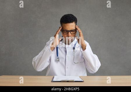 Junger afroamerikanischer Arzt, der an Kopfschmerzen leidet und am Schreibtisch sitzt Stockfoto