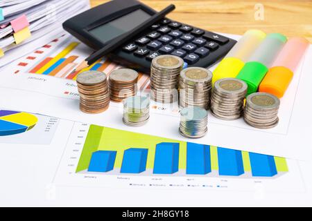 Der Münzstapel mit Business-Papier-Grafiken und Bleistift mit Diagrammen Bericht, Rechner Konzept der Berechnung von Ausgaben, Einkommen und Ausgaben. Stockfoto