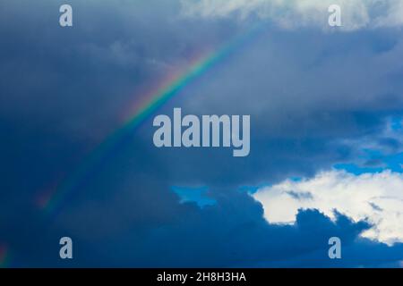Farbenfroher Regenbogen mit dunklen Sturmwolken vor dem Hintergrund des blauen Sommerhimmels. Konzept von Veränderung, Hoffnung. Stockfoto
