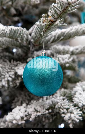 An einem frostigen Weihnachtsbaum hängt eine türkisblaue Glitzerkugel Stockfoto