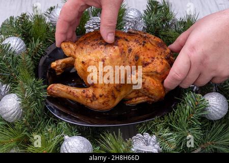 Traditionelles Weihnachtsessen. Hände schnitzen gebackenes Huhn, truthahn auf einem festlichen Tisch mit Fichtenzweigen und Weihnachtsdekorationen, Nahaufnahme. Hauskoch Stockfoto