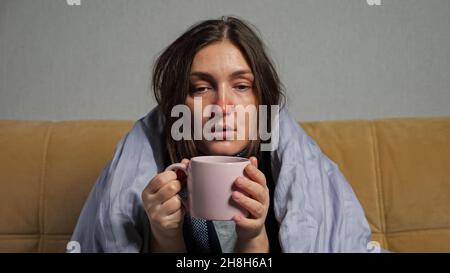 Frau erkrankt und trinkt Tee in einer Decke auf dem Sofa Stockfoto