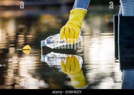 Freiwillige Abholung Plastikflasche aus verschmutztem See oder Meer. Wasserverschmutzung durch Plastikmüll. Umweltschäden Stockfoto