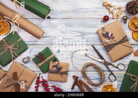 Geschenkschachteln für Weihnachten vorbereiten. Dekoration und eingewickelte weihnachtsgeschenke auf Holztisch. Flach liegend. Geschenkpapier, Schere und Weihnachtsschmuck Stockfoto