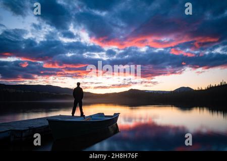 Stehende Silhouette beobachten den Sonnenuntergang am Horizont und seine Reflexion über dem See, Gaspesie, Quebec, Kanada Stockfoto
