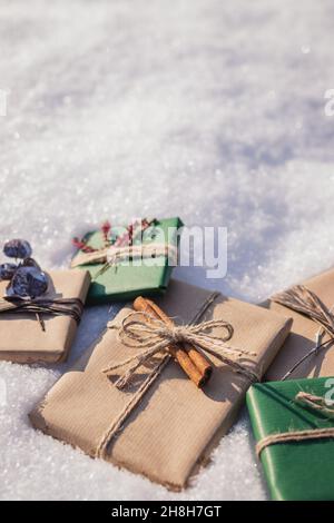 Eingewickelte Weihnachtsgeschenke mit Dekoration im Schnee. Geschenkschachteln aus grünem und braunem Kraftpapier Stockfoto