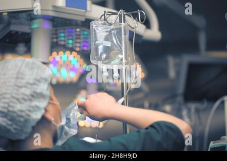 Krankenschwester, die die Lösungs-Beutel im Tropfsystem im Operationssaal ersetzt. Stockfoto
