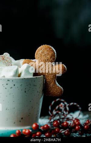 Nahaufnahme eines Lebkuchenkekse in einer Tasse Kaffee, gekrönt mit einigen Marschwalben mit verschiedenen Formen, auf einem grauen rustikalen Holztisch, gegen ein d Stockfoto