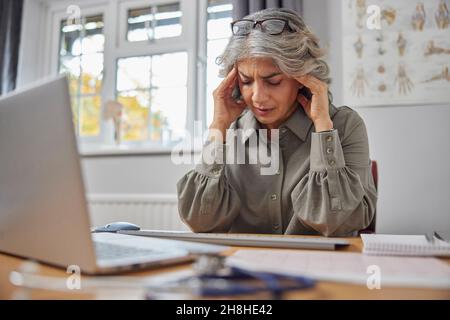 Gestresster und überarbeiteter reifer Hausarzt am Schreibtisch im Ärztebüro Stockfoto