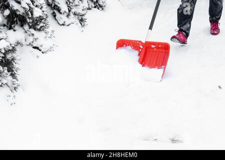 Beine Fuß unkenntlich Person in Turnschuhen mit roter Schaufel. Reinigung Schnee im Hof. Entfernt Schnee von der Straße. Winter. Schneeverwehungen. Stockfoto