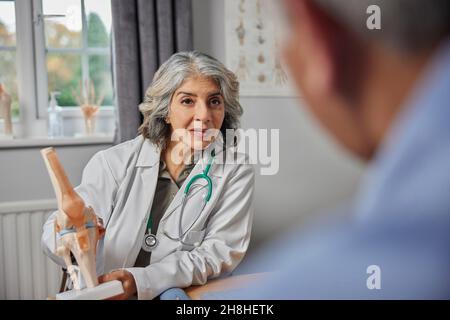 Reifer Weiblicher Doktor Treffen Mit Männlicher Patient Diskussion Gelenkschmerzen In Knie Mit Anatomisches Modell Stockfoto