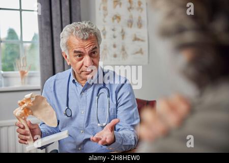 Reifer Männlicher Arzt Treffen Mit Weiblicher Patient Diskussion Gelenkschmerzen In Der Schulter Mit Anatomischen Modell Stockfoto