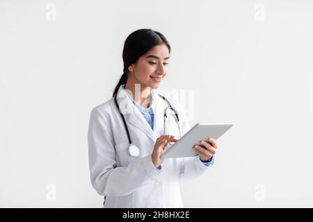 Lächelnde junge hindu-Frau Arzt in weißem Mantel Arbeit auf Tablette, isoliert auf weißem Hintergrund Stockfoto