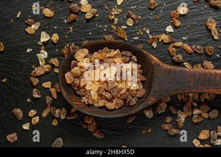 Holzlöffel voll dunkelbraunem Granulatzucker auf Schieferhintergrund aus nächster Nähe. Stockfoto