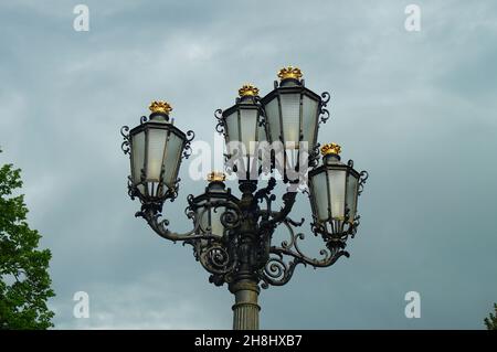 HANAU, DEUTSCHLAND - 13. Mai 2021: Straßenlaterne im Schlosspark Philippsruhe, Hanau, Deutschland im Frühjahr gegen einen unruhigen Himmel. Vergoldete Kronen. Stockfoto