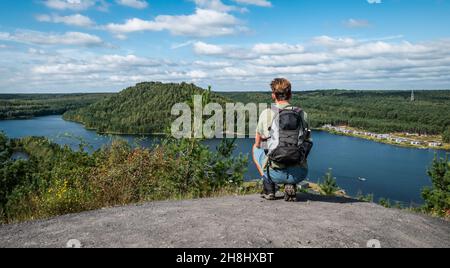Junger männlicher Backpacker, der auf einem Felsen hockt und die wunderschöne Panoramalandschaft genießt. Stockfoto