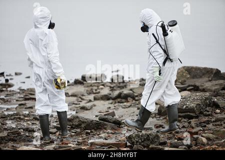 Porträt von zwei Arbeitern in Gefahrgutanzügen, die Probenproben mit Wasser und giftigen Abfällen sammeln Stockfoto