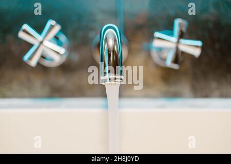 Händewaschen im Waschbecken zu Hause. Nahaufnahme öffnen Chrom Metall Silber Wasserhahn mit weißer Keramik-Badewanne in Luxus Bad Wand Hintergrund Stockfoto