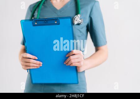 Nahaufnahme einer nicht erkennbaren Ärztin in grüner medizinischer Uniform mit Klemmbrett, die auf weißem, isolierten Hintergrund im Studio steht. Stockfoto