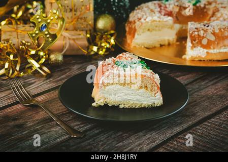 Roscon de reyes mit cremefarbenen und weihnachtlichen Ornamenten auf einem Holztisch. Kings Day Concept spanish Three Kings Cake.Traditional Spanish Epiphany Cake.Typ Stockfoto