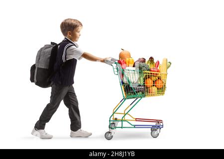 In voller Länge Profilaufnahme eines Jungen in einer Schuluniform, der einen Mini-Einkaufswagen mit Obst und Gemüse auf weißem Hintergrund isoliert schiebt Stockfoto