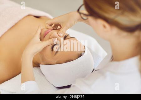 Weibliche Kosmetikerin, die eine Gesichtsmassage für Gäste macht, die im Beauty Center oder Spa liegen. Stockfoto