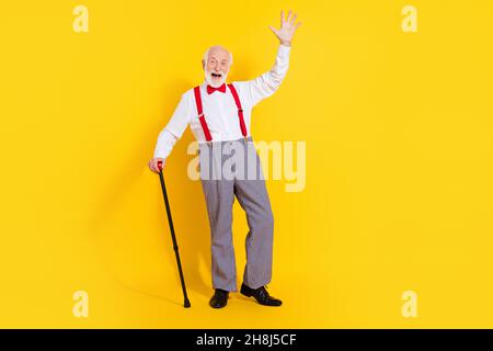 In voller Länge Foto von lustigen älteren Mann mit Stick tragen Krawatte weißes Hemd rote Hosenträger karierte Hose Schuhe auf gelbem Hintergrund isoliert Stockfoto