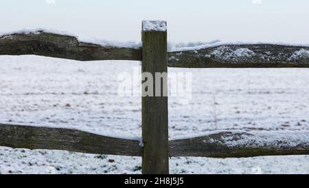 Pfosten- und Schienenzäune am Rand des Ackerlandes, das von einem Stauben von Schnee bedeckt ist. Stockfoto