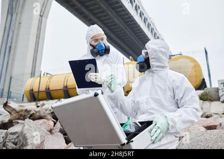 Portrait von zwei Wissenschaftlern, die Hazmat-Anzüge tragen, die Proben im Freien sammeln, toxischer Abfall und Schadstoffkonzept Stockfoto