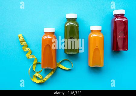 Bunte frische Säfte oder Cocktails aus Obst und Gemüse in Flaschen auf blauem Hintergrund mit Maßband. Das Konzept einer gesunden Ernährung, Ernährung. Detox. Stockfoto