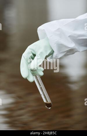 Nahaufnahme eines nicht erkennbaren Wissenschaftlers, der einen Hazmat-Anzug trägt und Wasserproben sammelt, mit Handschuhen und Reagenzglas Stockfoto