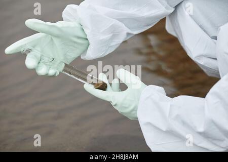 Nahaufnahme eines nicht erkennbaren Wissenschaftlers, der einen Hazmat-Anzug trägt und Wassersonden sammelt, mit Handschuhen, die das Reagenzglas halten, fokussieren Stockfoto