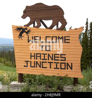 Schild für Haines Junction im Südwesten des Yukon, Kanada. Das Holzschild zeigt eine Figur, die einen Grizzlybären darstellt. Stockfoto