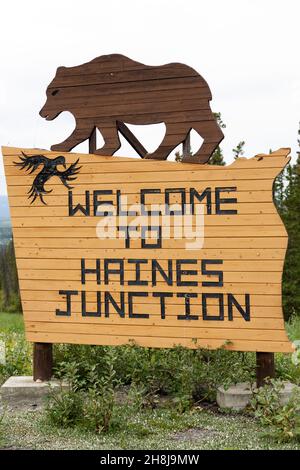 Schild für Haines Junction im Südwesten des Yukon, Kanada. Das Holzschild zeigt eine Figur, die einen Grizzlybären darstellt. Stockfoto