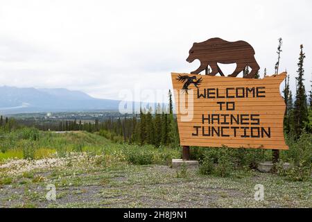 Schild für Haines Junction im Südwesten des Yukon, Kanada. Das Holzschild zeigt eine Figur, die einen Grizzlybären darstellt. Stockfoto