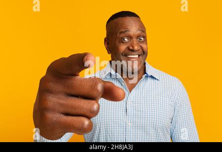 Fröhlicher reifer afroamerikanischer Mann, der mit dem Zeigefinger auf die Kamera auf orangefarbenem Studiohintergrund zeigt Stockfoto