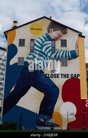 Mailand, Italien farbenfrohe Wandgraffiti. Street-Art-Wandgemälde des Künstlers Rosk, das einen jungen Mann zeigt, der eine Wand mit der Botschaft „Close the Gap“ schiebt. Stockfoto