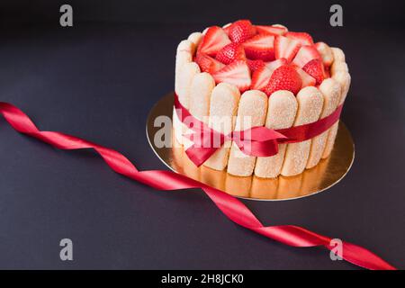 Tiramisu-Kuchen mit Erdbeeren, Marienkäfer, Mascarpone und rotem Schleifband auf Schwarz. charlotte-Kuchen Stockfoto