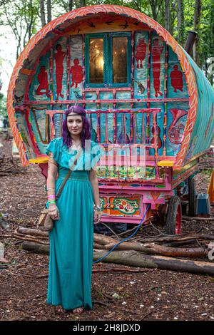 Junge unkonventionelle Hippie-Mädchen, die vor traditionellen Zigeunerwagen oder Karren im Wald stehen. Stockfoto